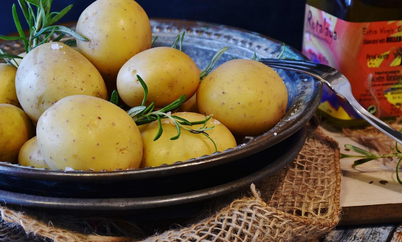 patate intere da pelare su un piatto nero con rosmarino sopra